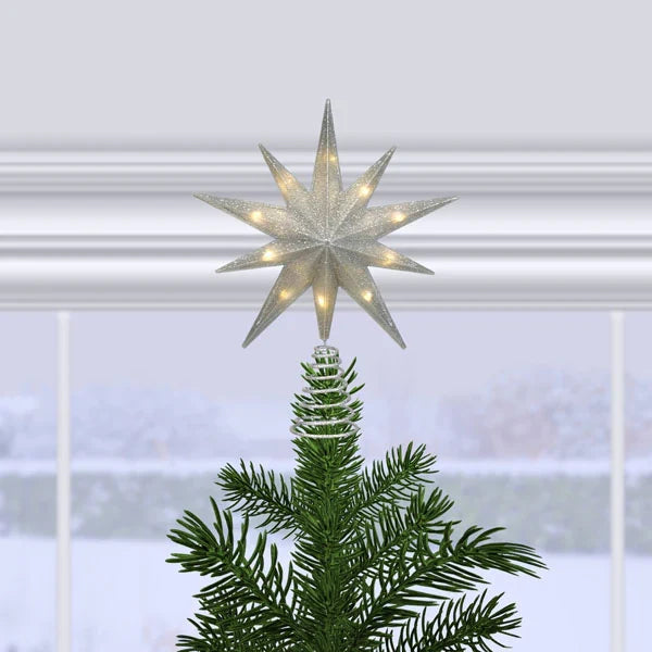 12" silver glitter star treetop lit on a Christmas tree in front of a snowy window scene.