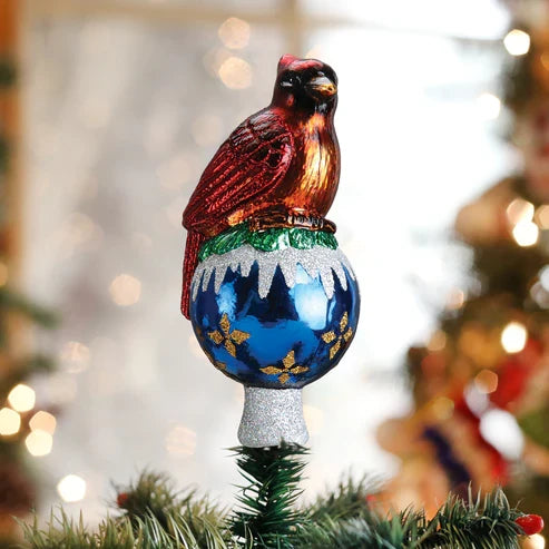 Red cardinal tree topper displayed on top of a decorated Christmas tree with warm lights in the background.