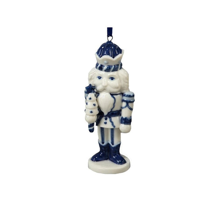 Blue and white nutcracker ornament in a Delft-inspired style holding a stacked tree and standing on a round base with a blue ribbon hanger.