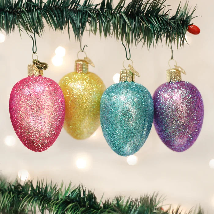 Four glittery Egg Shaped Christmas ornaments in pink, yellow, blue, and purple hanging on a tree branch.
