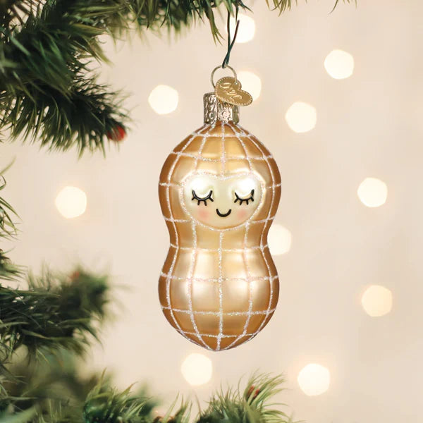 Decorative Christmas ornament shaped like a peanut with a smiling face, hanging on a tree with lights in the background.