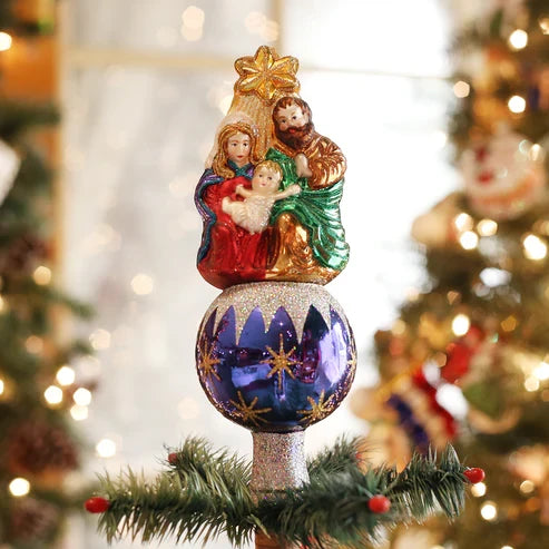 Nativity tree topper displayed on top of a decorated Christmas tree with warm lights in the background.