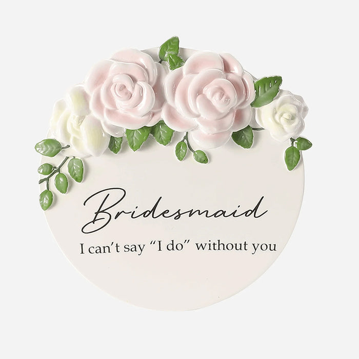 Round white ornament with pink and white roses, green leaves, and text 'Bridesmaid I can't say I do without you' on a white background.