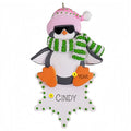 Decorative penguin ornament with a pink hat, green and white scarf, and personalized name on a white background.