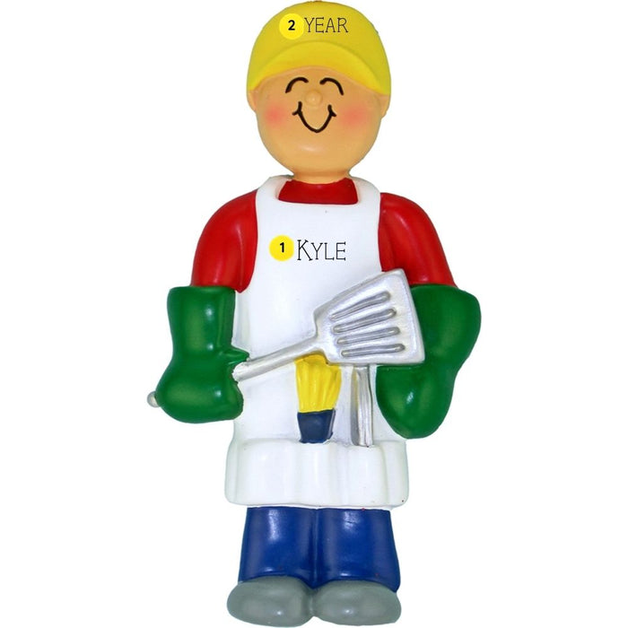Ornament of a person in a yellow hat and red shirt holding a spatula, personalized with name and year on an apron, on a white background.