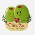 Two green olives with faces and a heart, labeled 'Olive You' ornament, on a beige base with text.