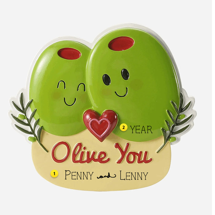 Two green olives with faces and a heart, labeled 'Olive You' ornament, on a beige base with text.