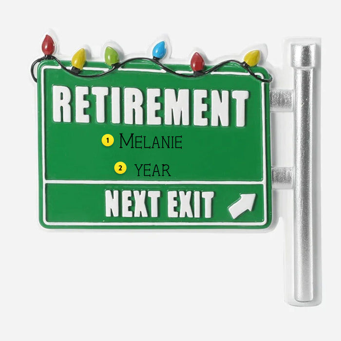 Green road sign ornament with 'Retirement' and 'Next Exit' text, decorated with colorful lights on a white background.