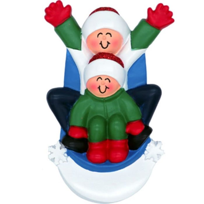 Decorative ornament of two people sledding on a blue sled with white snow at the bottom.
