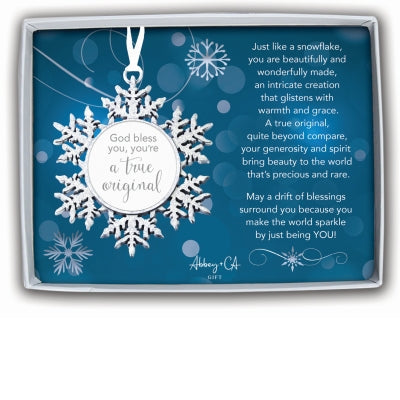 White snowflake ornament with ribbon hanger and round center tag reading “God bless you, you’re a true original,” displayed in a gift box with blue sentiment card.